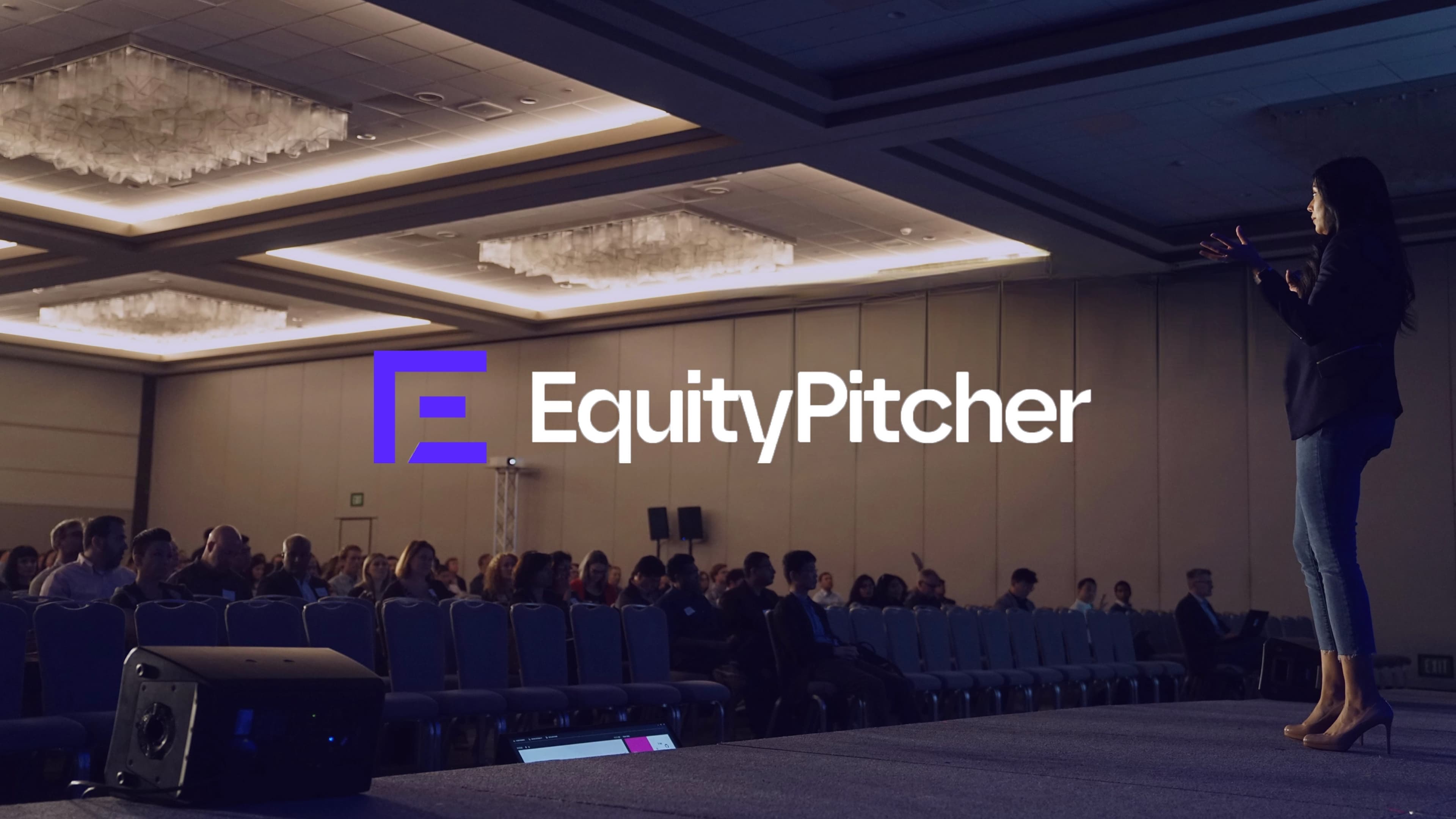 The EquityPitcher logo on a conference stage screen as a speaker addresses the audience