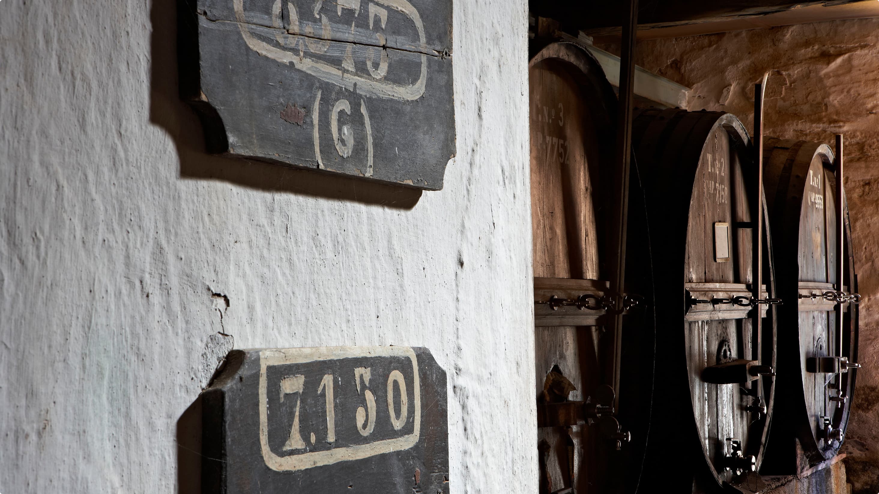 Numbered plaques on a whitewashed wall beside wine barrels in the Quinta Vale D. Maria cellar